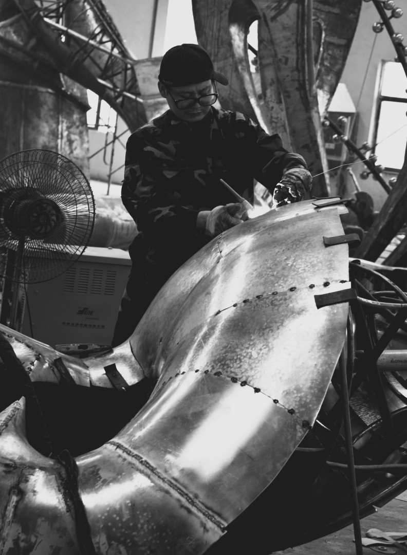A craftsperson working on the metal surface of Bridge of Winds.
