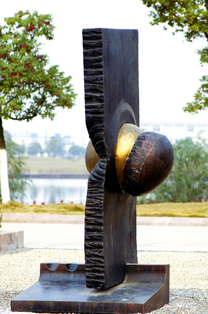Sphere in Slab, a bronze sphere breaking through a vertical slab