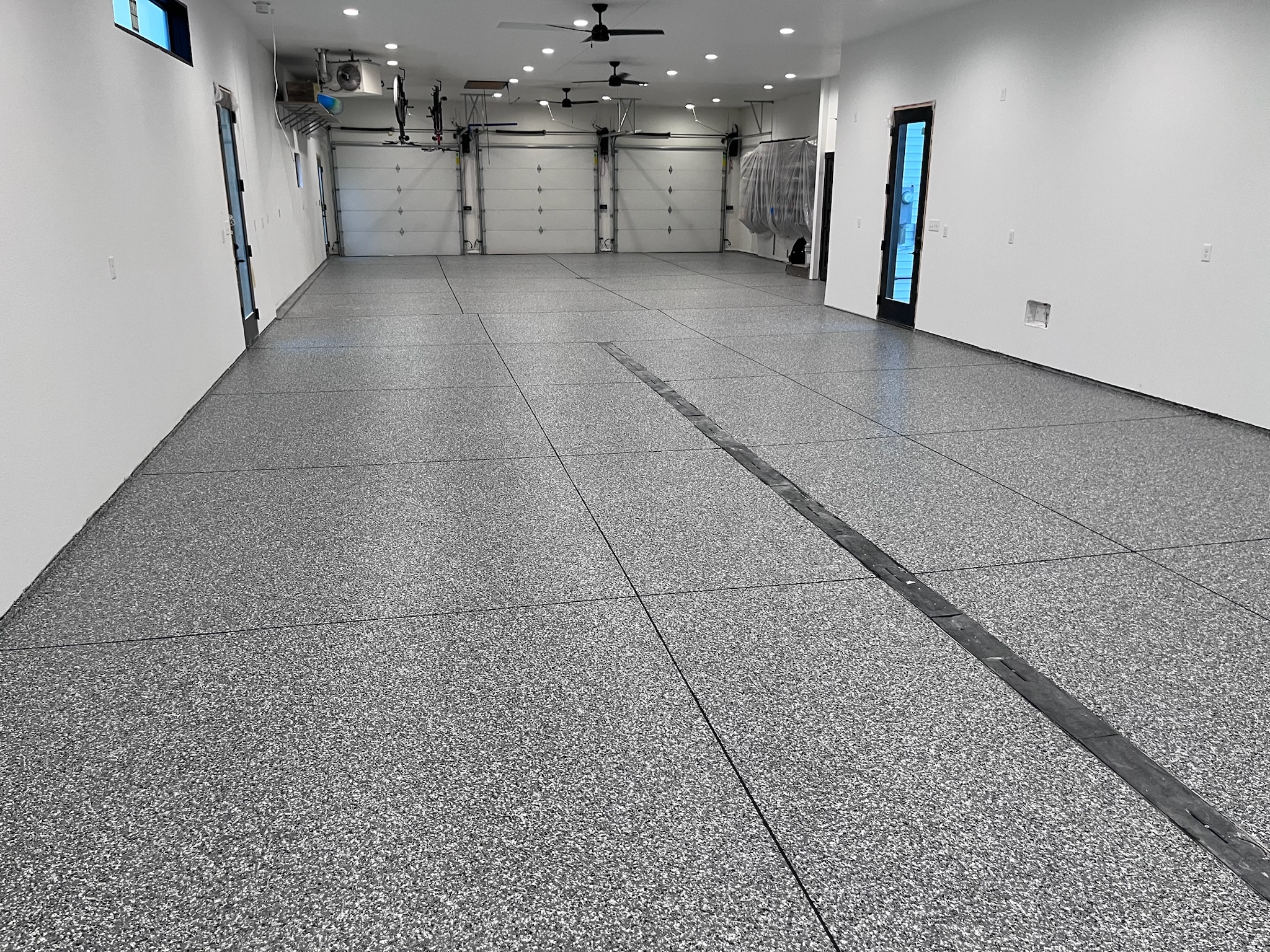 Large garage with full broadcast epoxy floor, three overhead doors, and white walls with two black-framed doors in Bismarck, ND.