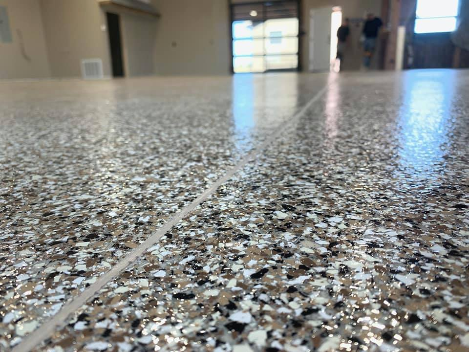 Close-up of full broadcast epoxy flooring with white, black, and gray flakes reflecting light indoors in Mandan ND.
