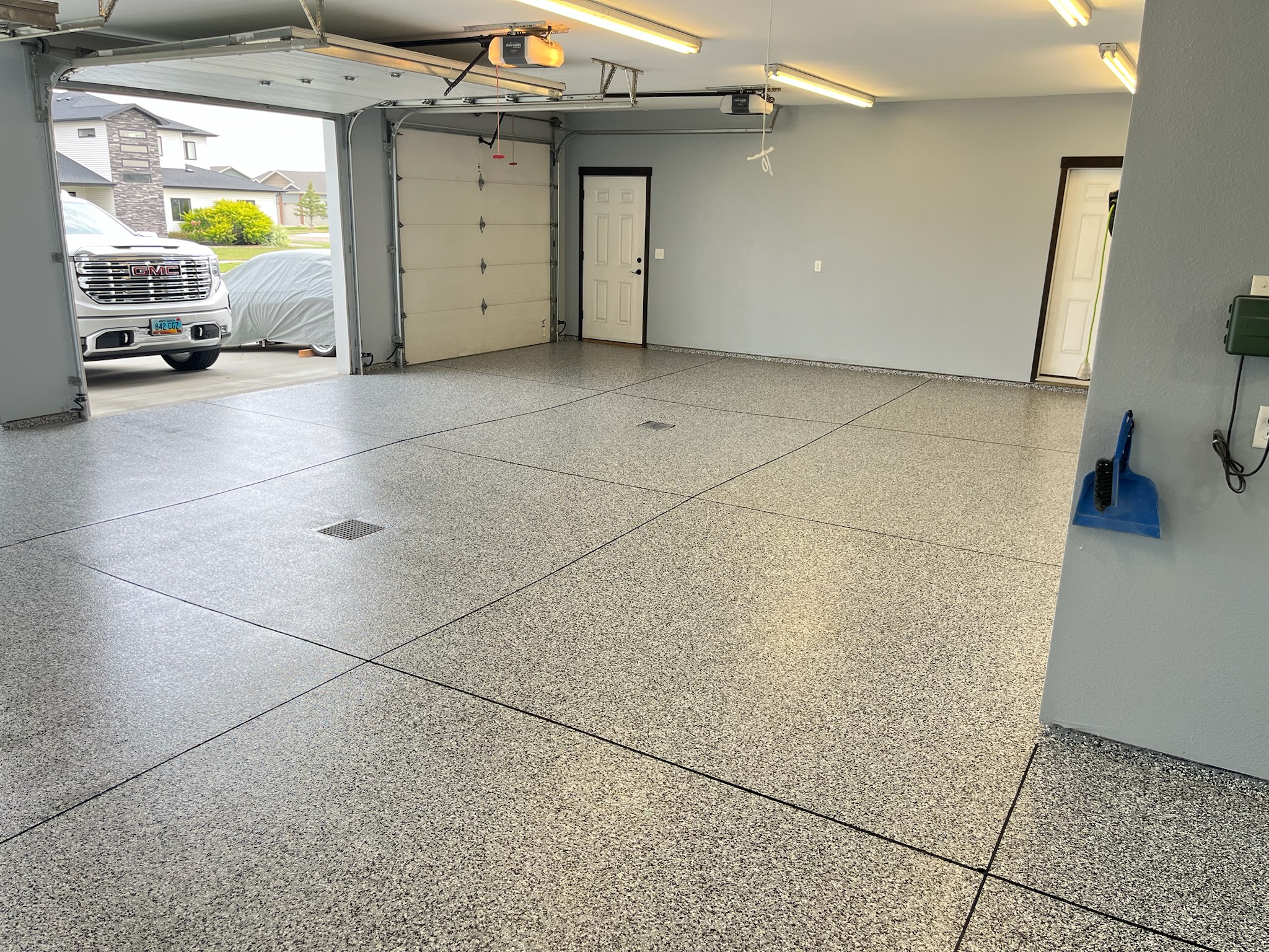 Interior of a clean garage with full broadcast gray epoxy coated floor, open door showing a white GMC truck and covered car outside.