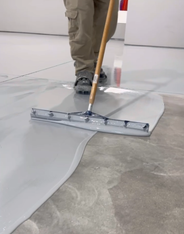 Person in work boots professionally spreading gray epoxy on a concrete floor in Bismarck, ND