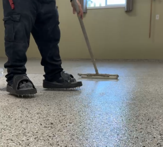 Person wearing black spiked shoes professionally installing polyaspartic topcoat on a full broadcast floor.