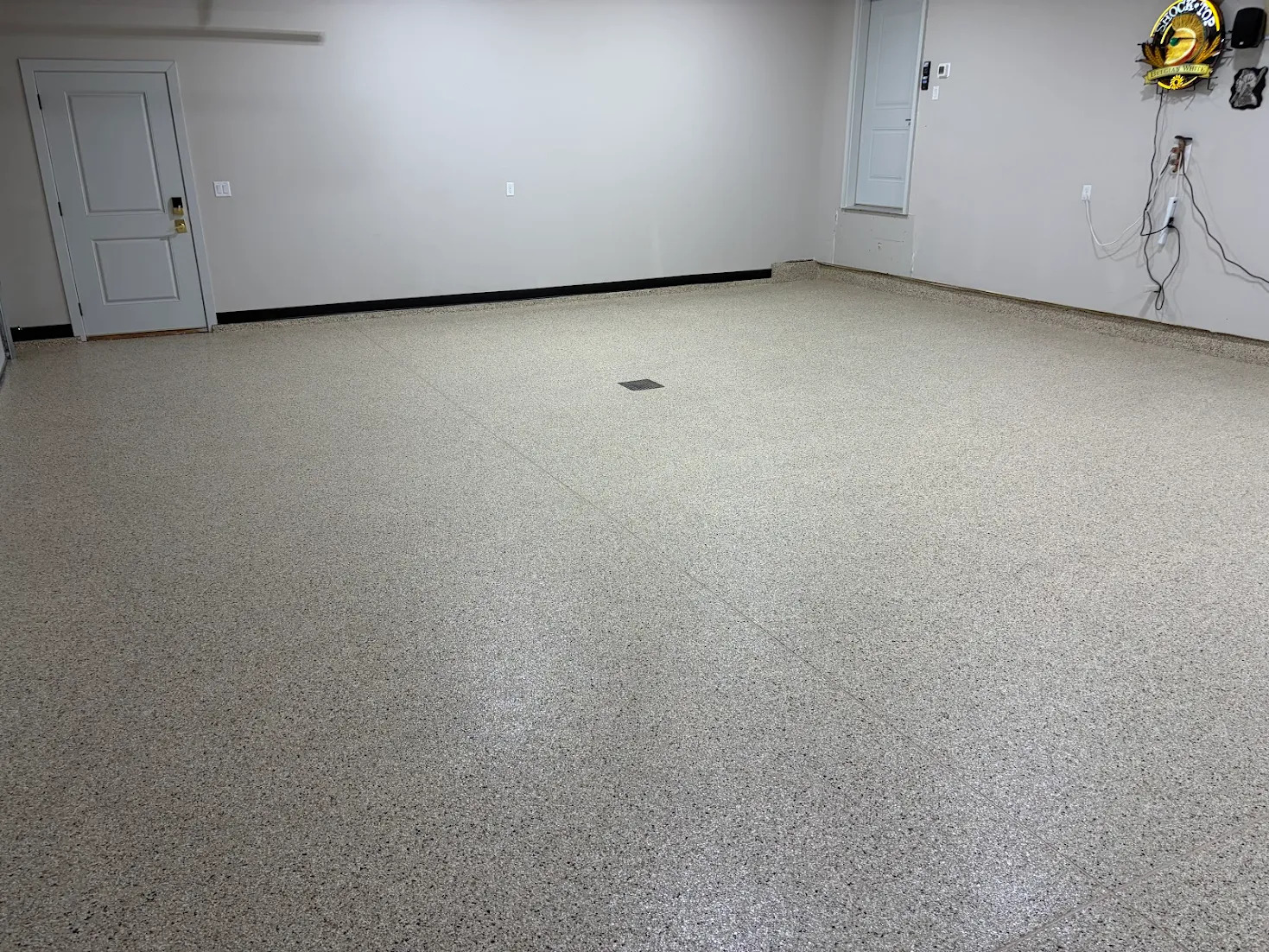 Empty clean garage with full broadcast professionally installed epoxy floor, white walls, and two closed grey doors.