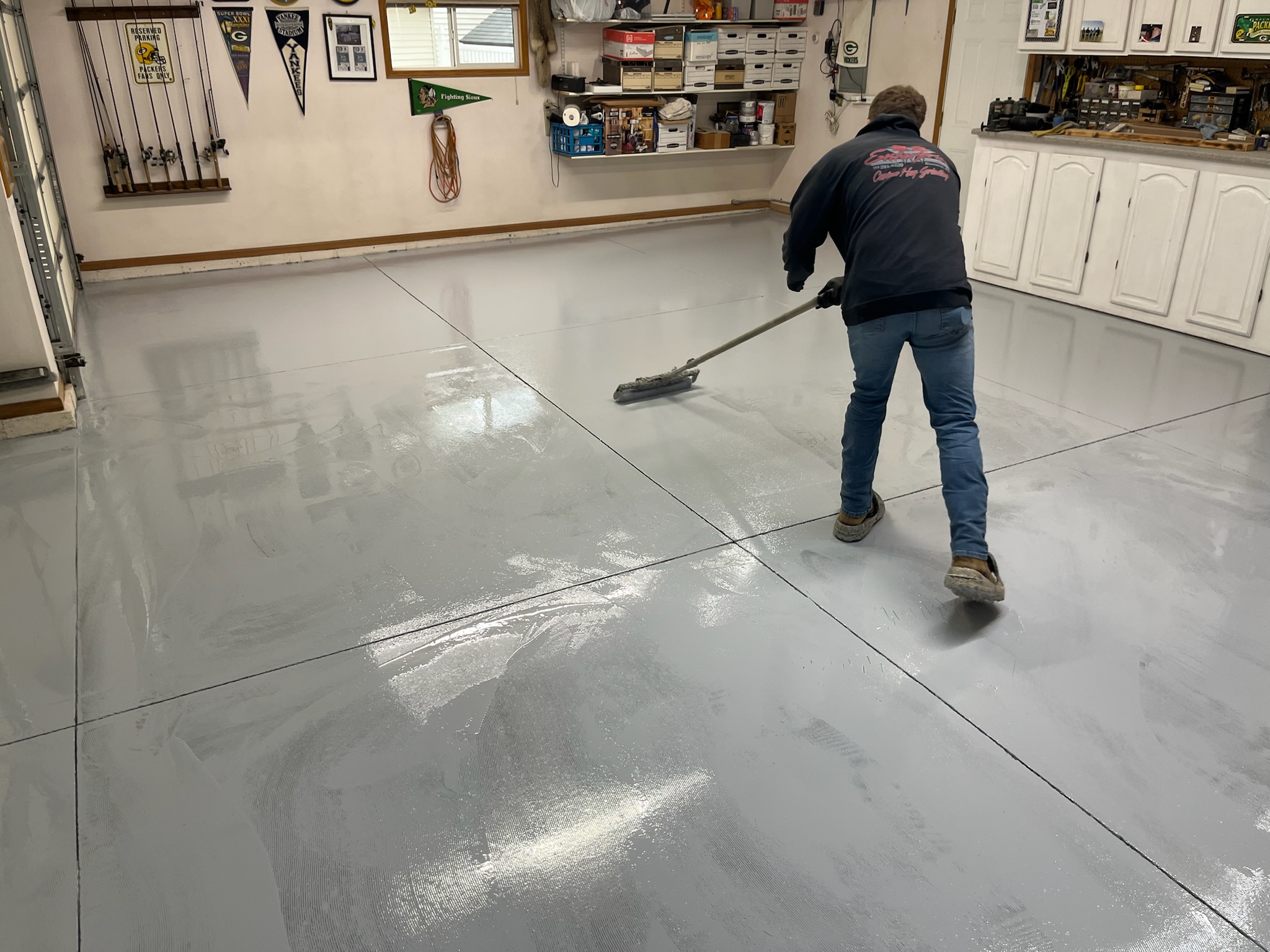 Armour Floors employee professionally applying a gray coating to a garage floor with a roller.