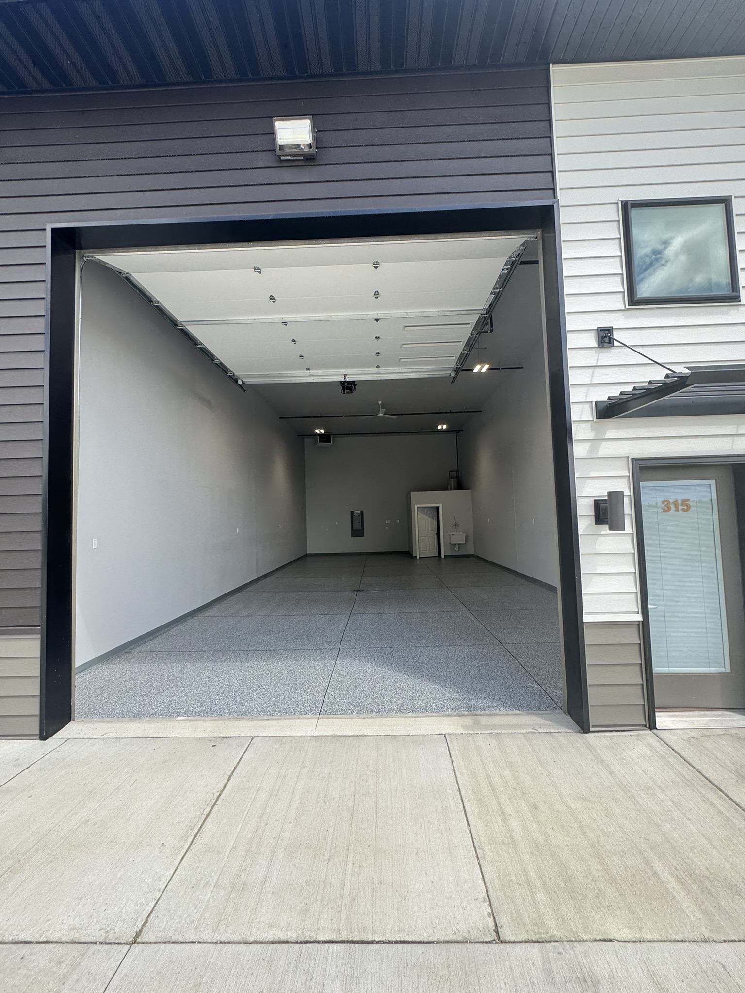 Empty Paradise Valley, Bismarck, ND Shop Condo with professionally installed epoxy floor, white walls, and overhead door open.