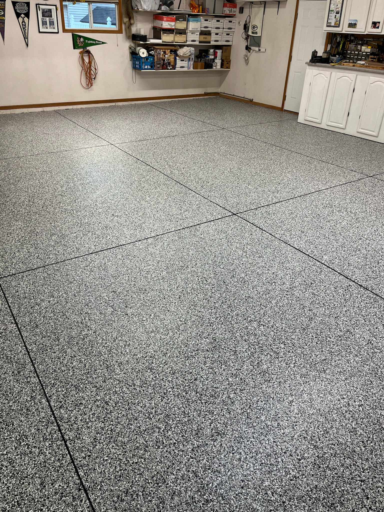 Clean garage with full broadcast flake epoxy-coated floor, white cabinets, and wall shelves with tools and storage boxes in Bismarck, ND.
