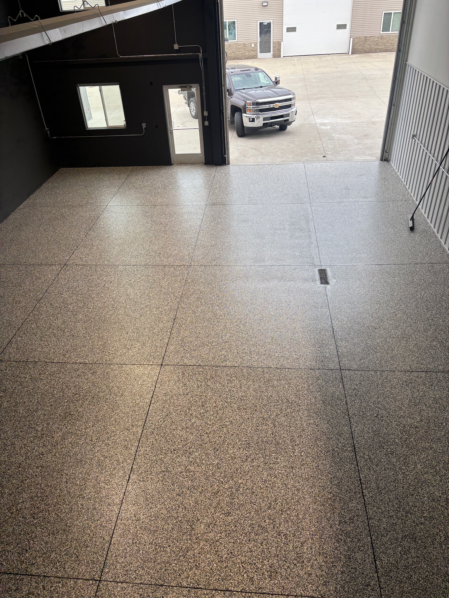 Clean empty shop in Mandan ND with speckled epoxy flooring and a gray pickup truck outside on concrete.
