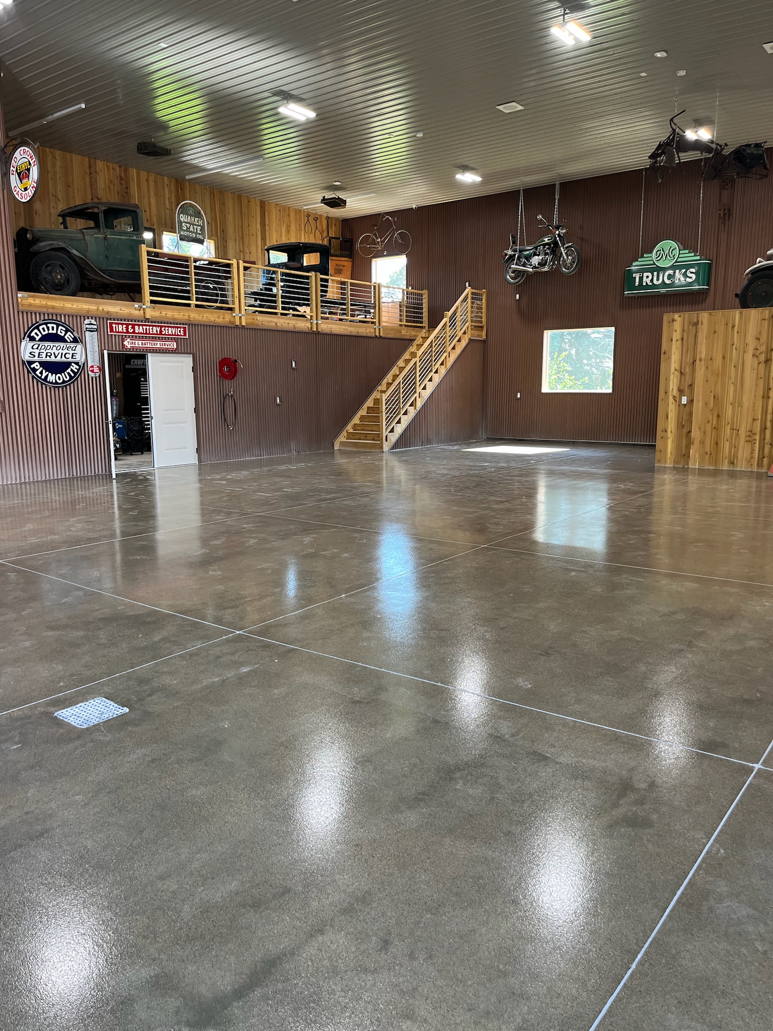 Spacious garage with polished concrete floor, vintage vehicles on balcony, and motorcycle suspended from ceiling.