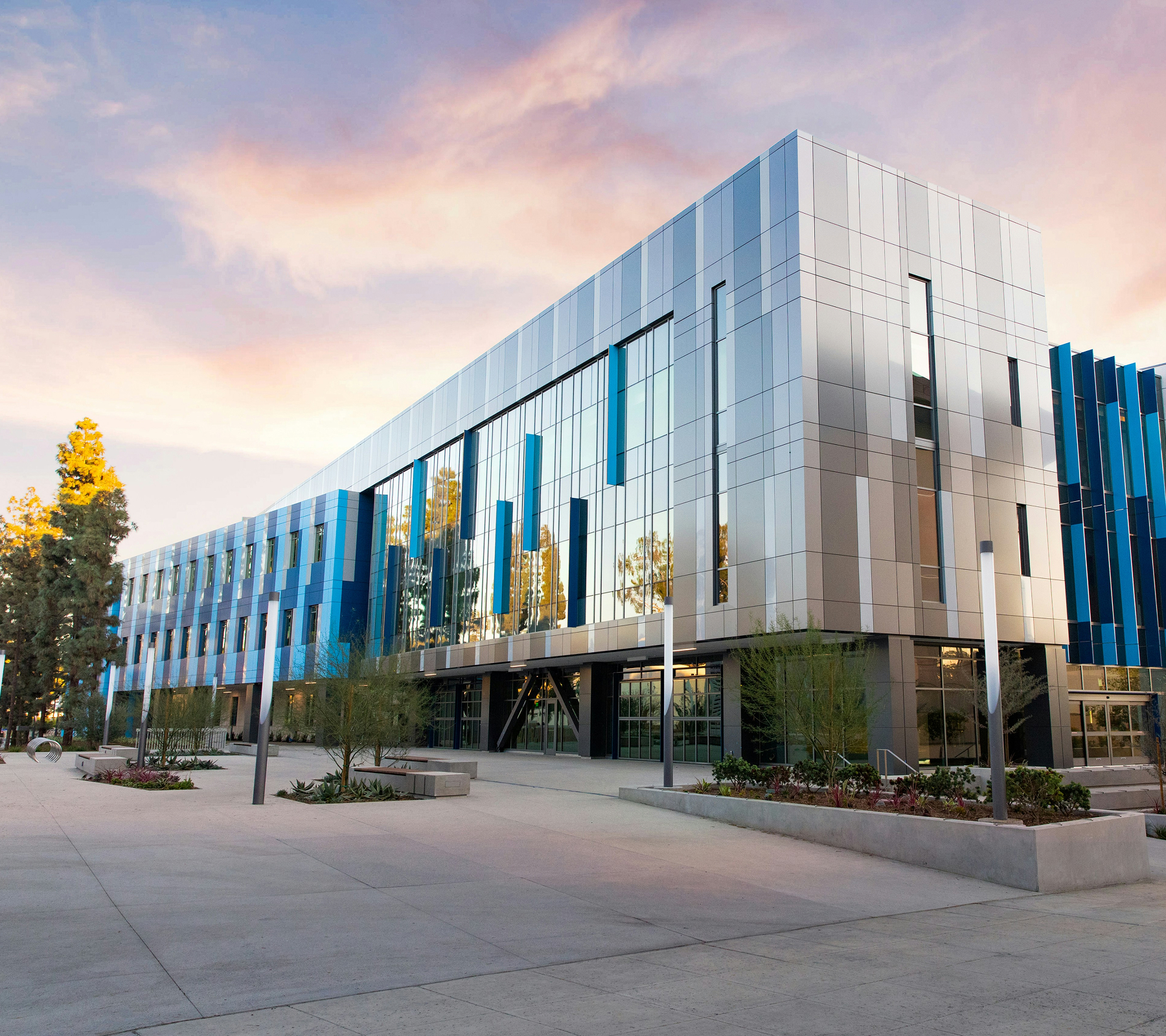 Modern three-story building with reflective glass windows and blue-gray panels at sunset.