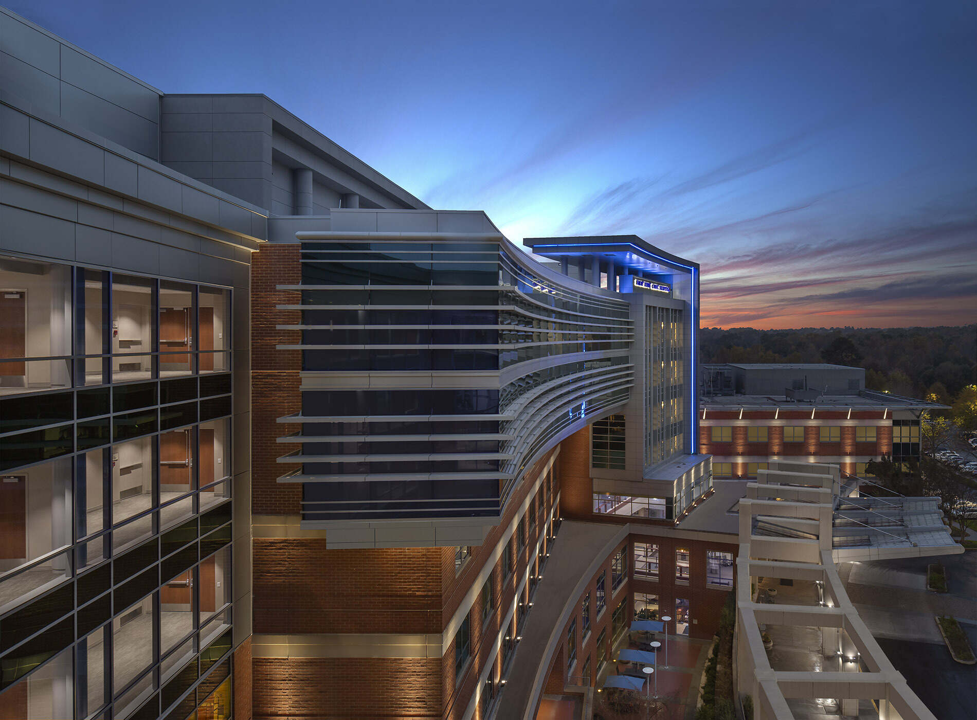 Modern building with glass, white beams, and blue lighting under dusk sky with clouds.