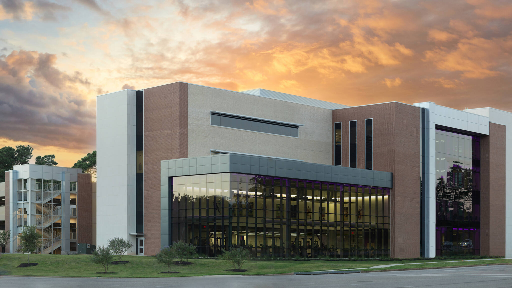 Modern three-story building with large glass windows and a sunset sky background.