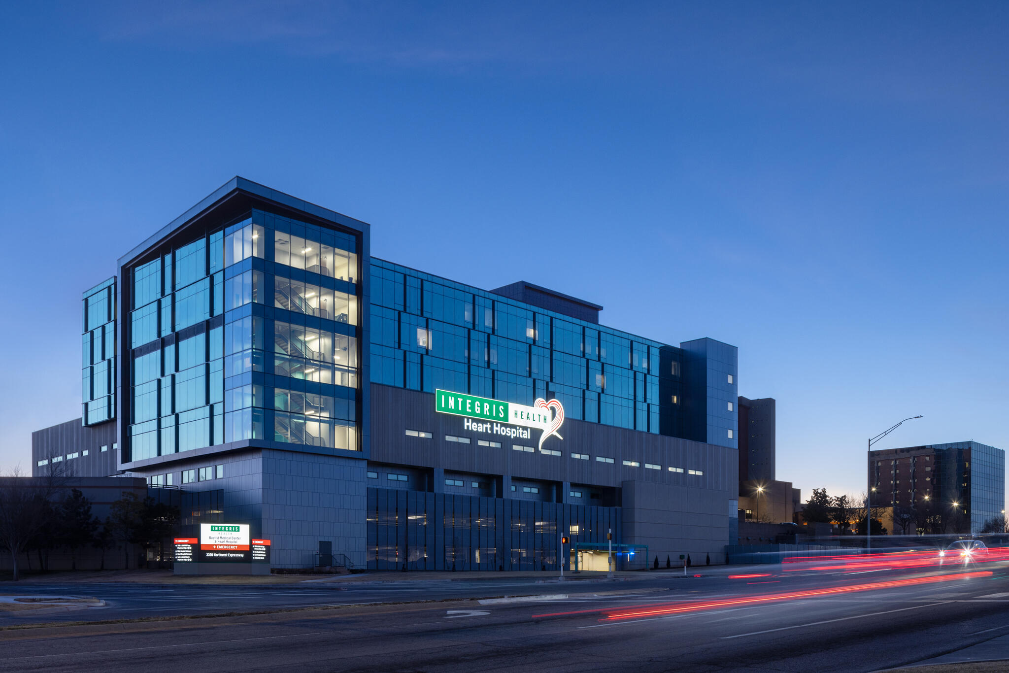 Modern glass and concrete Integris Health Heart Hospital building at dusk with light trails on the street.