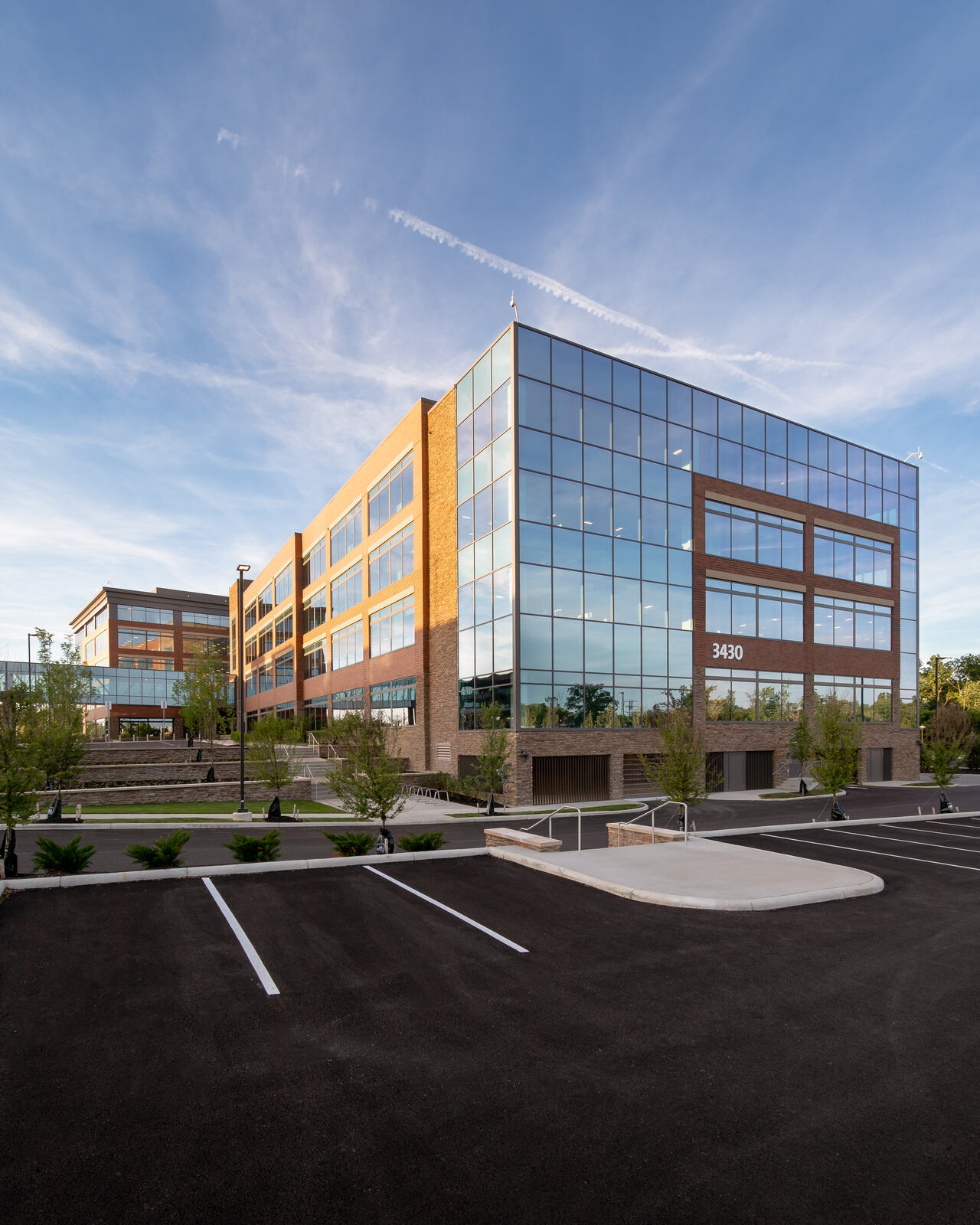 Modern office building with glass and brick exterior reflecting blue sky and empty parking lot.