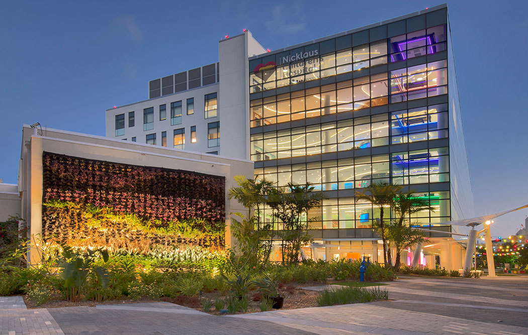 Exterior of a modern hospital building with large glass windows and a vertical garden wall at dusk.