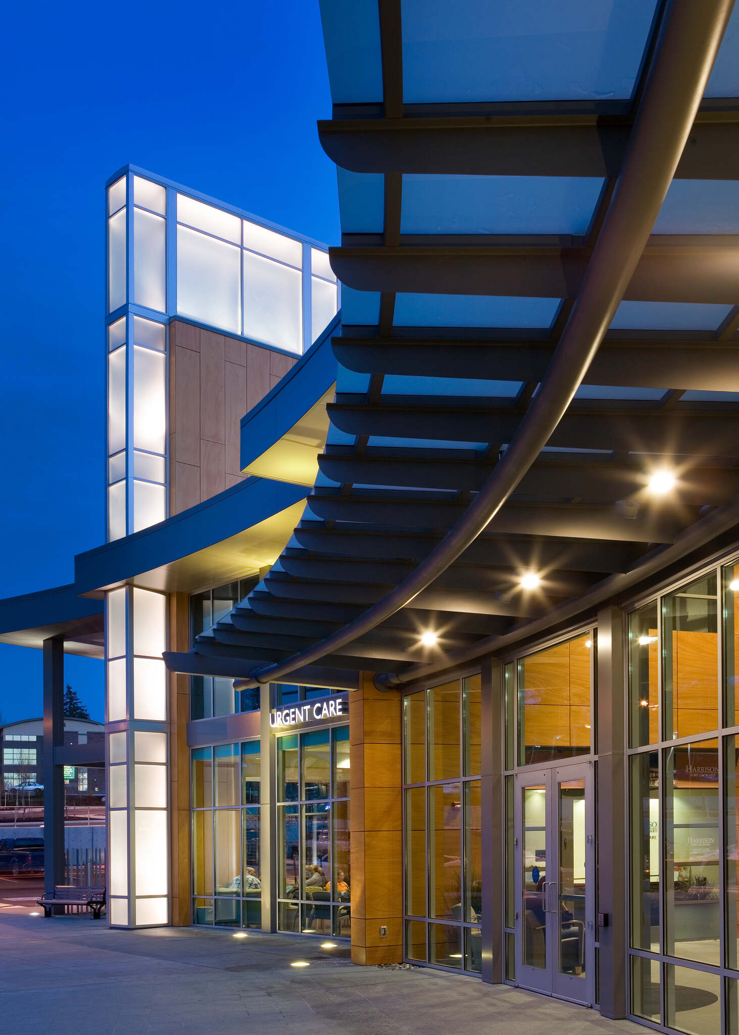 Modern urgent care building entrance with curved overhang and illuminated glass panels at dusk.