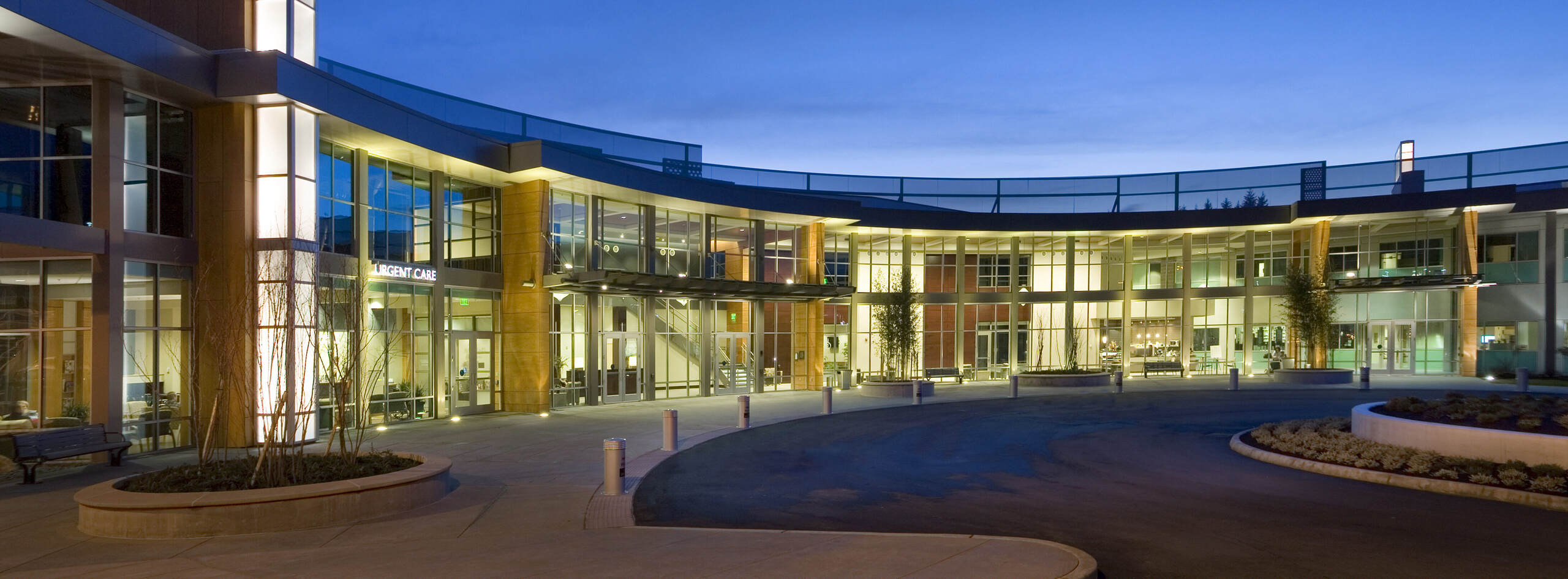 Modern medical office building at dusk with large glass windows and illuminated urgent care sign.