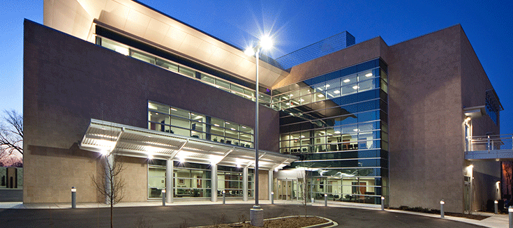 Modern building with large glass windows and outdoor lights at dusk.