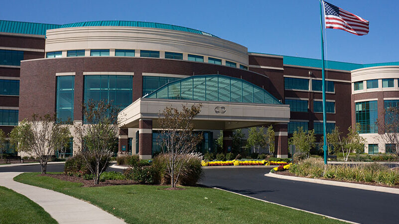 Modern brick building with large glass windows, an American flag, and landscaped entrance.