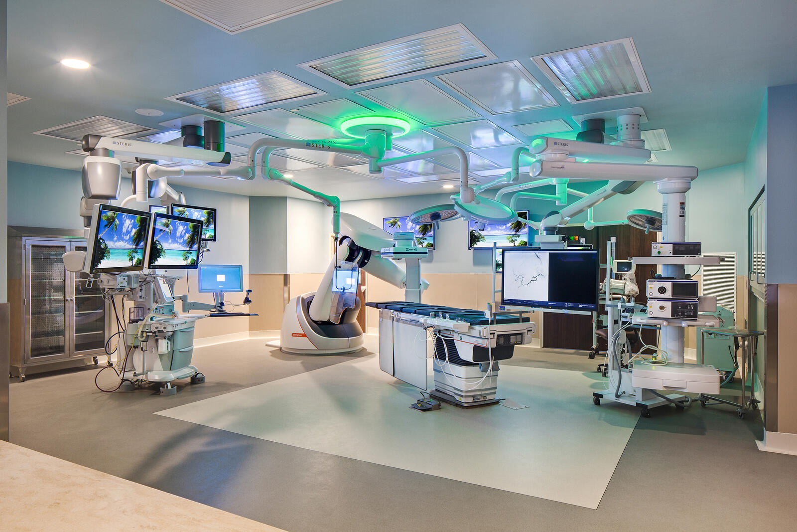 Modern operating room with surgical table, robotic arms, multiple monitors, and medical equipment.
