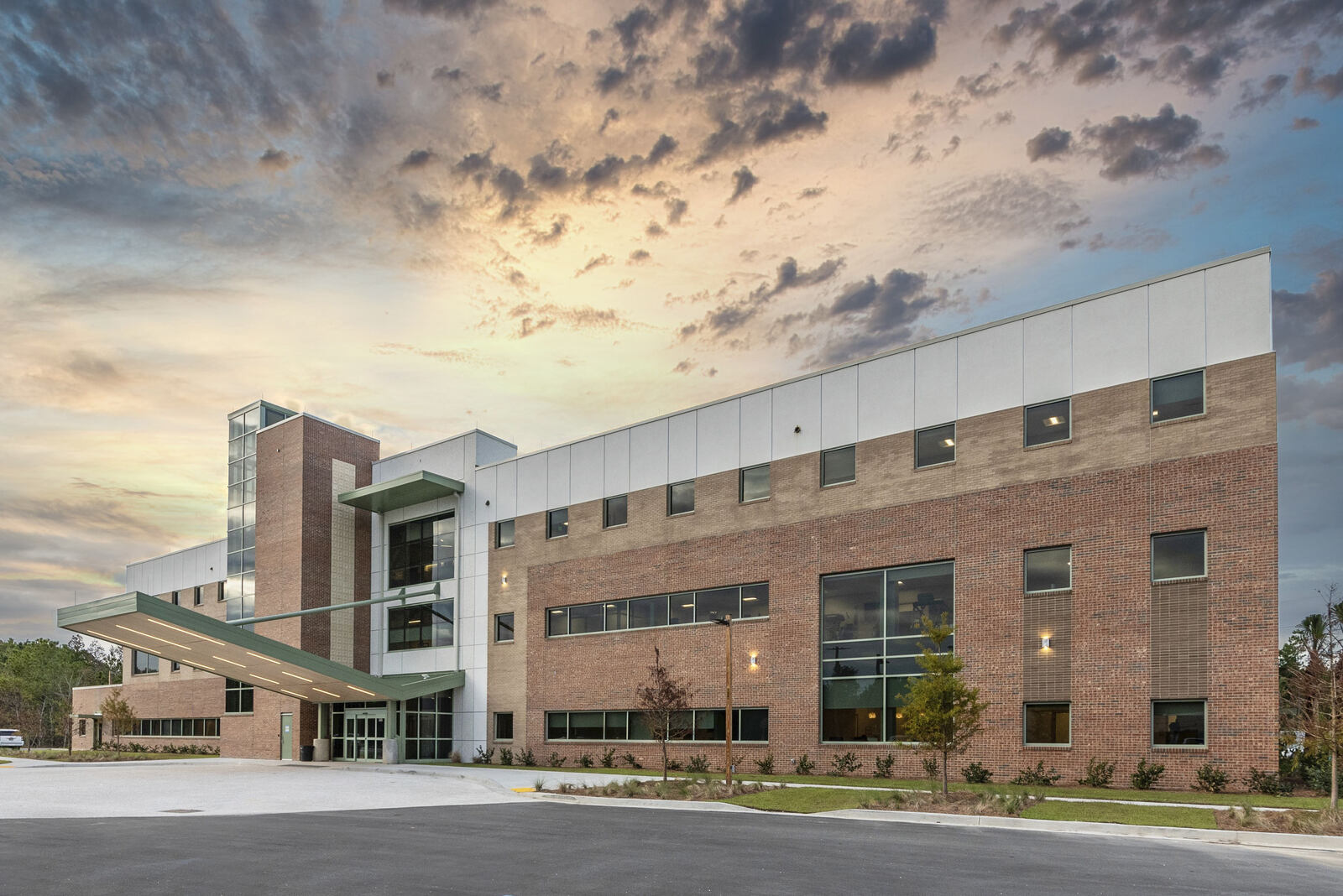 Modern three-story brick and glass building at dusk with dramatic cloudy sky.