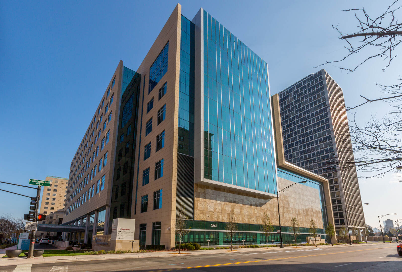 Modern multi-story building with glass facade and stone details at intersection under clear blue sky.