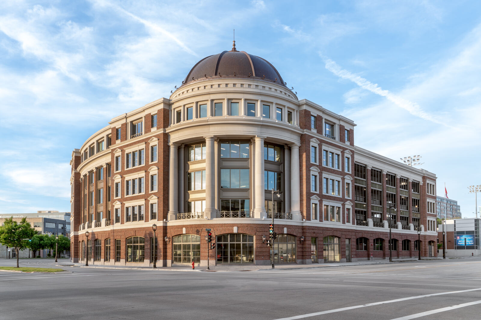 Large four-story red brick and stone building with a dome, columns, and many windows on a street corner.