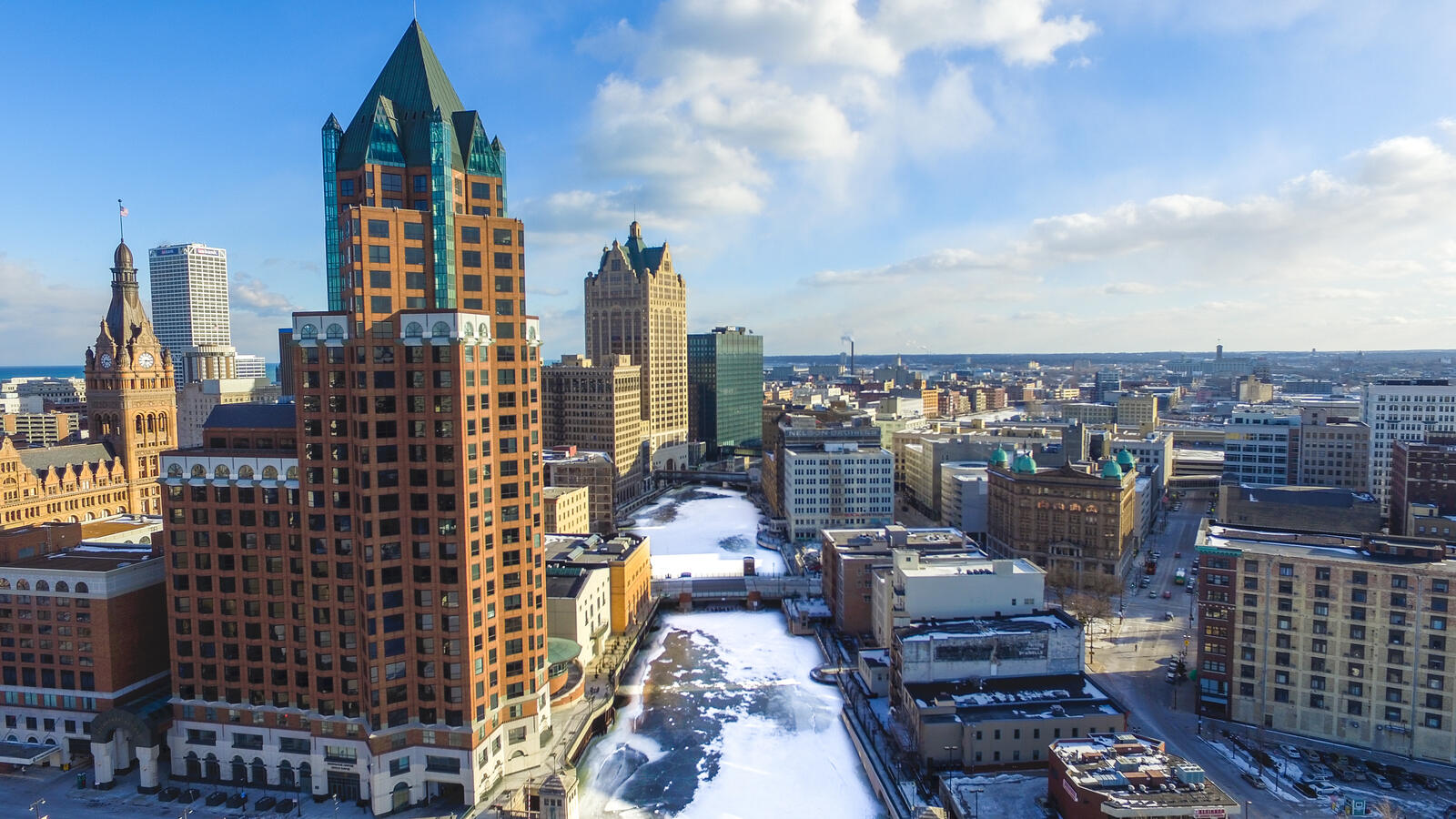 Aerial view of downtown Milwaukee with tall buildings and a partially frozen river on a clear day.