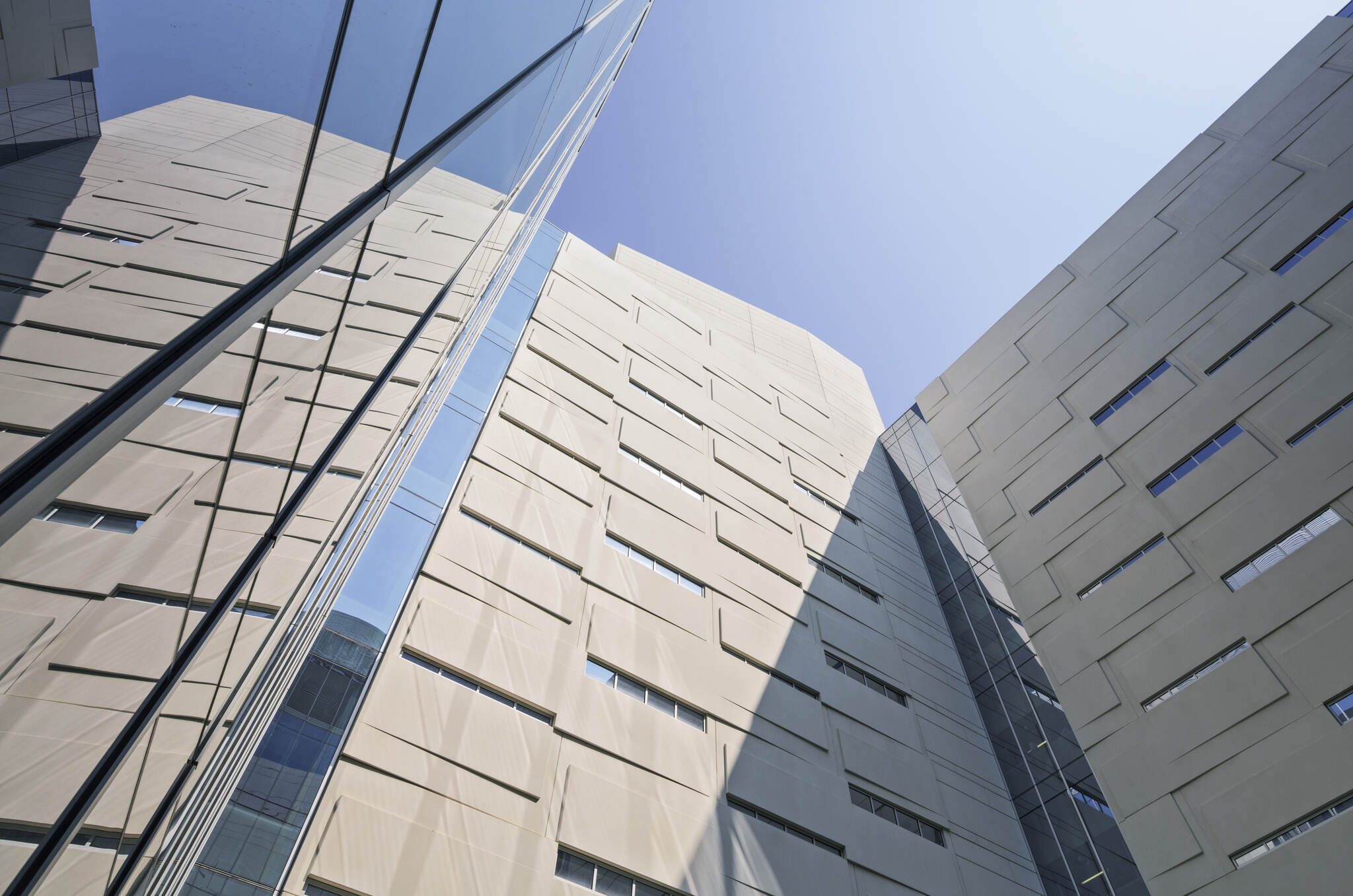 Upward view of modern beige building with reflective glass windows against clear blue sky.