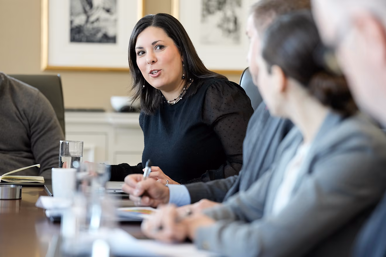 Woman speaking during a business meeting with colleagues sitting around a conference table.