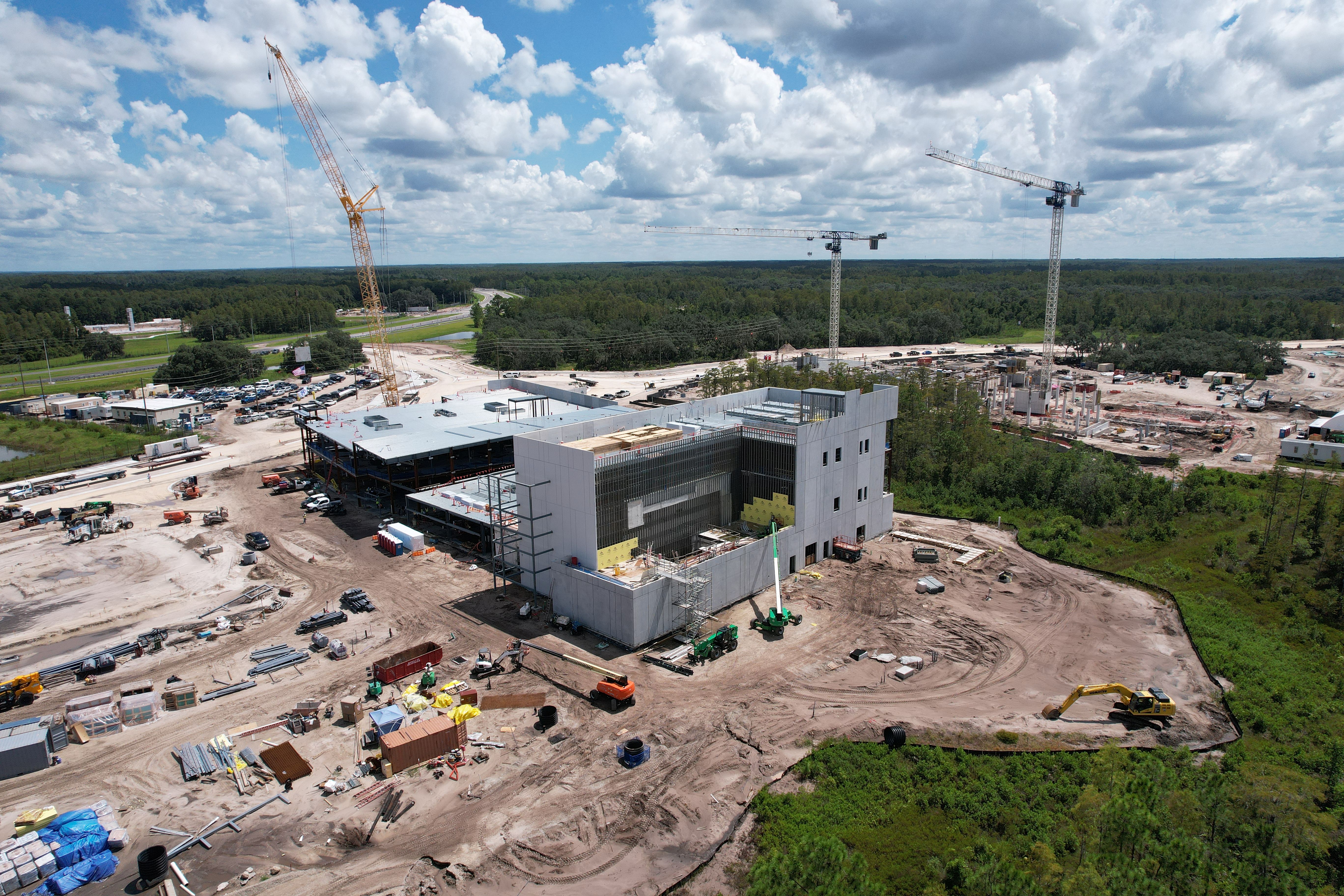 Aerial view of a large construction site with cranes and partially built structures amid a forested area.