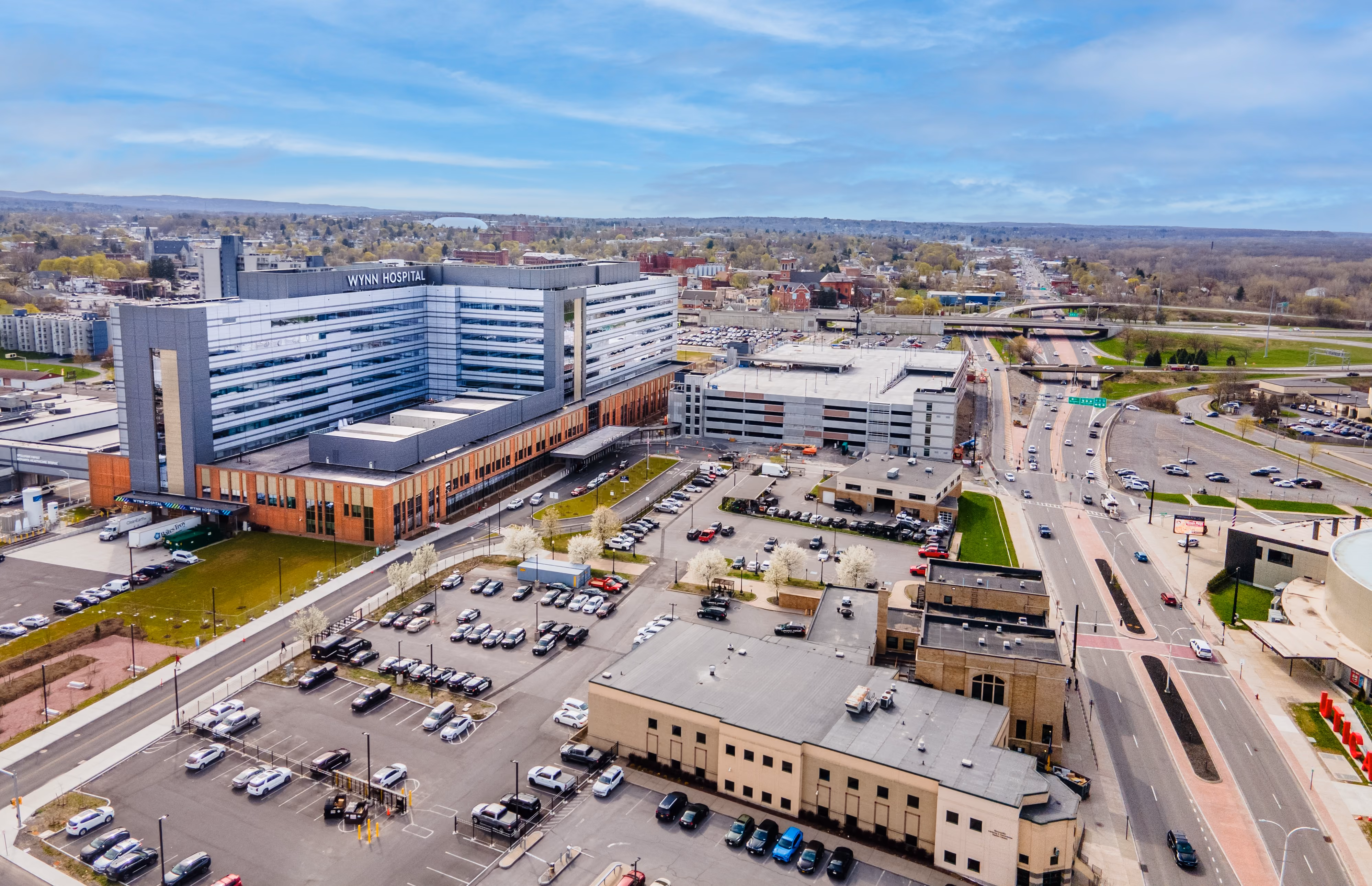 Aerial view of Wynn Hospital surrounded by parking lots and roads in a suburban area under a blue sky.