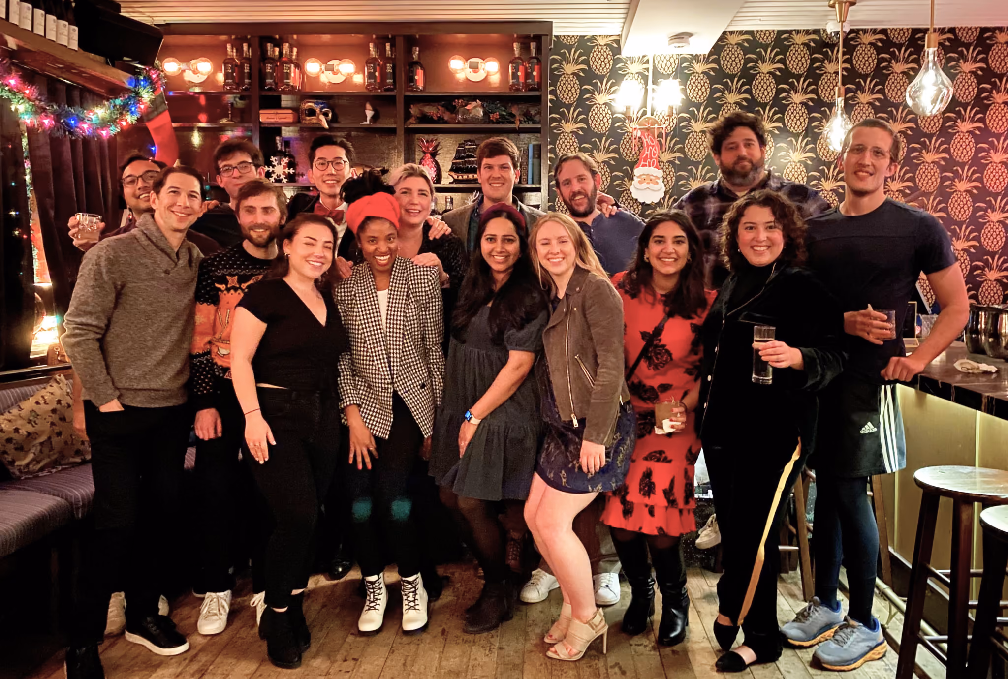 Group of people smiling and posing together in a warmly lit bar decorated with holiday lights and festive ornaments.
