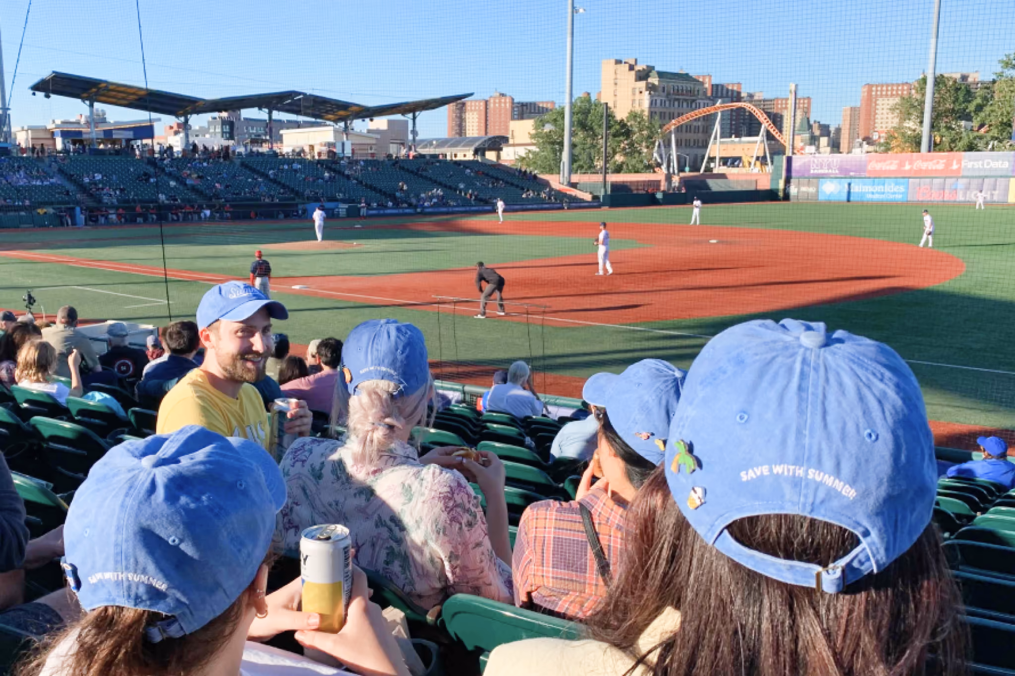 Spectators wearing blue caps watching a baseball game in a stadium on a sunny day.