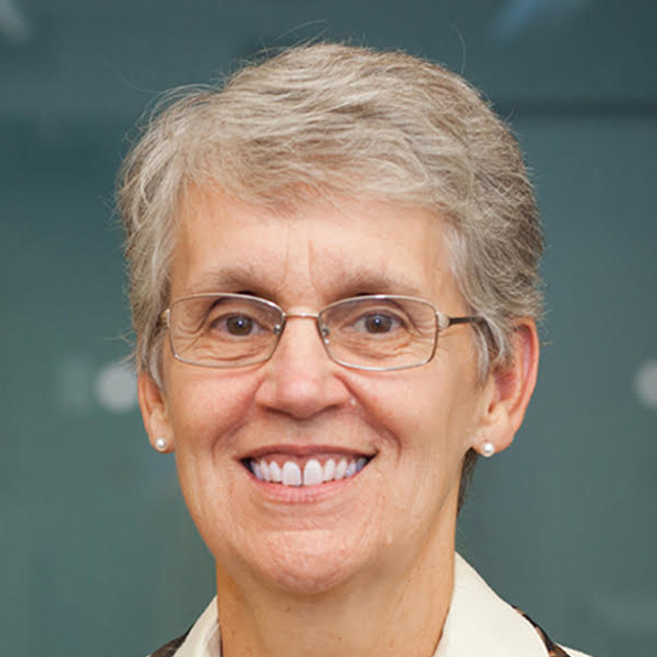 Smiling older woman with short gray hair, glasses, and pearl earrings wearing a light-colored top.
