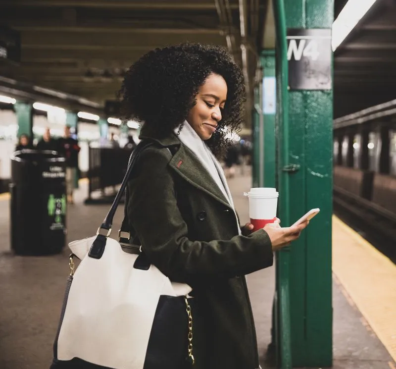 A woman looking at her phone, waiting for the subway