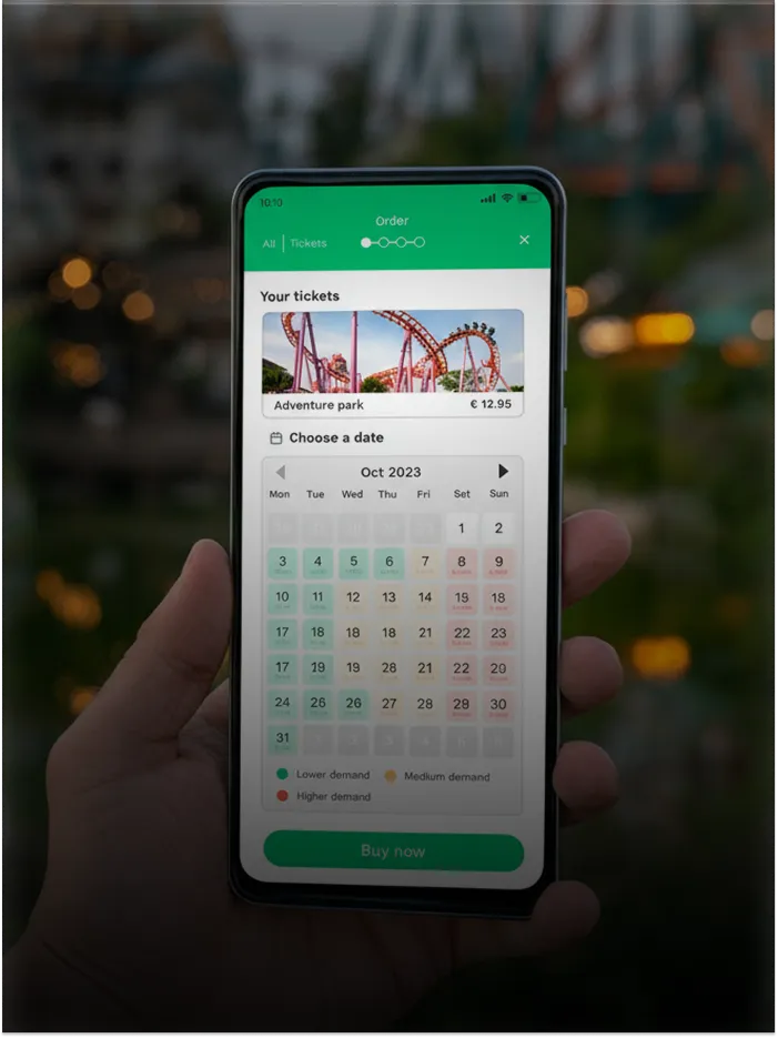 Hand holding phone showing amusement park ticket purchase app with a date calendar and demand levels.