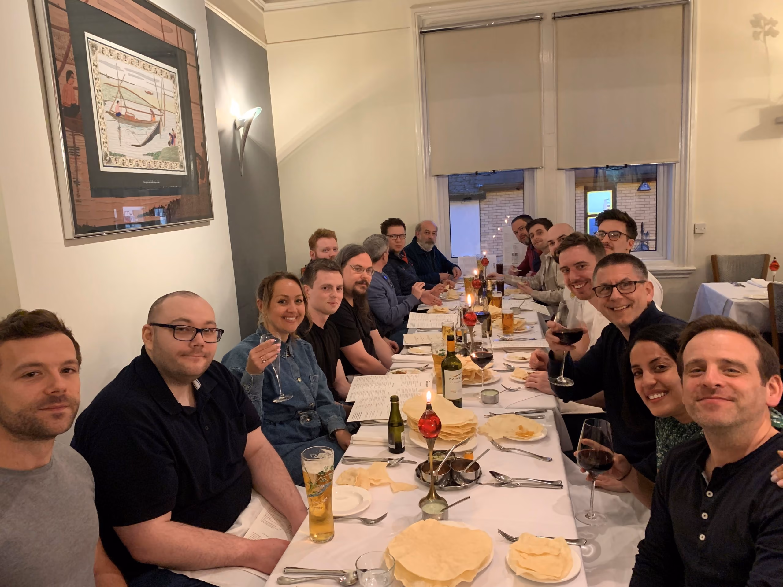 Group of people sitting at a long dining table with drinks and menus in a warmly lit room.