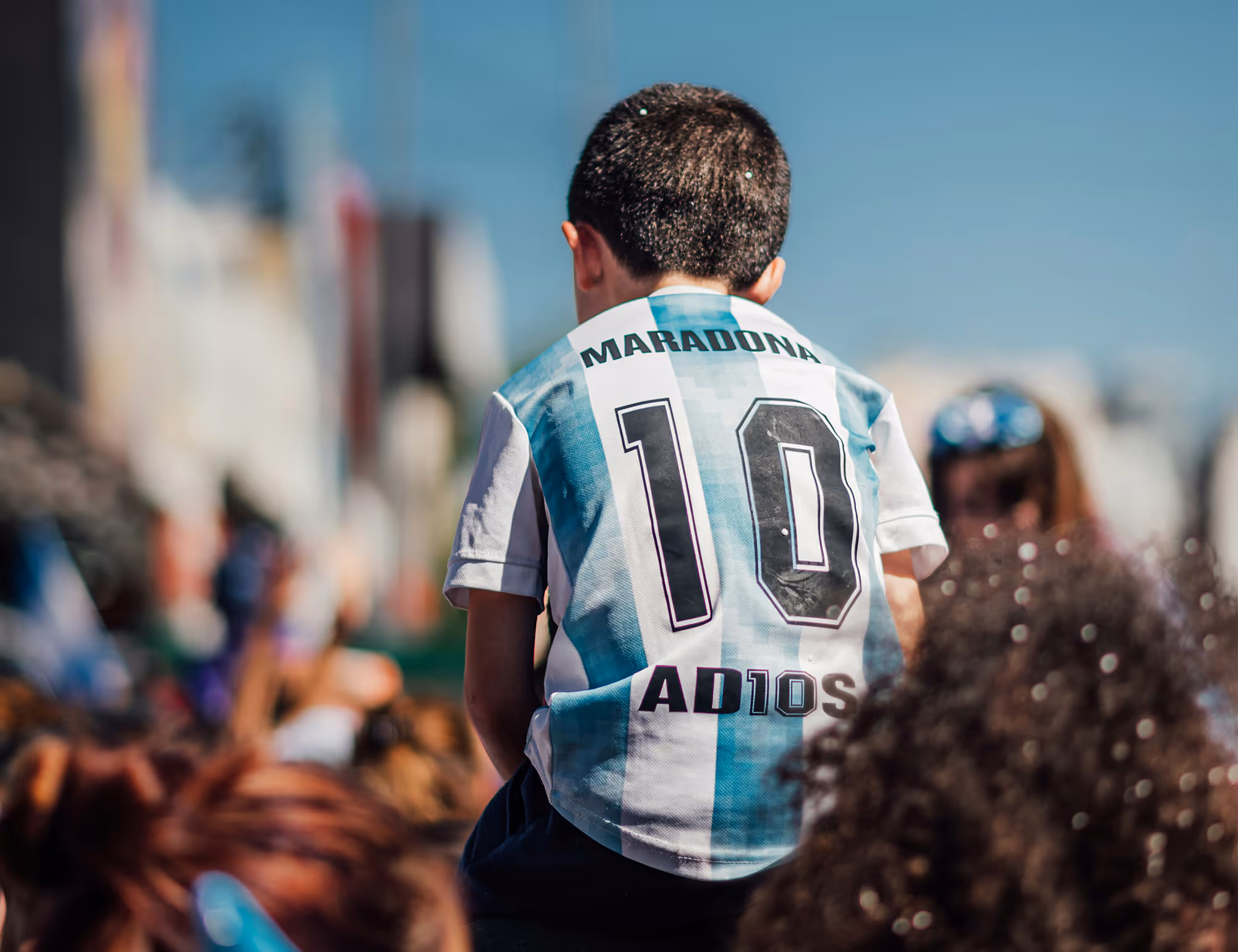 Child wearing Argentina soccer jersey with Maradona 10 and AD10S on back at outdoor event.