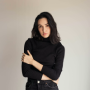 Woman with long dark hair wearing a black turtleneck, arms crossed, looking at the camera.