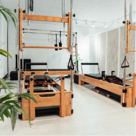 Modern Pilates studio with wooden reformer machines, white walls, and plants in a bright room.