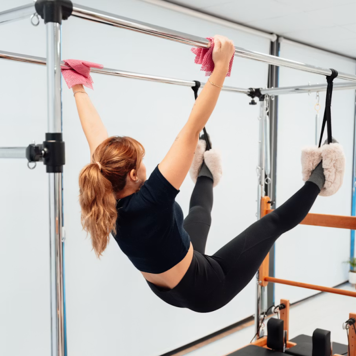 Woman exercising on Pilates reformer machine holding a metal bar with gloves, legs in straps.