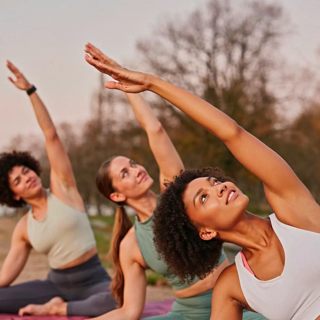 Three women doing side stretch yoga outdoors on mats in a park.