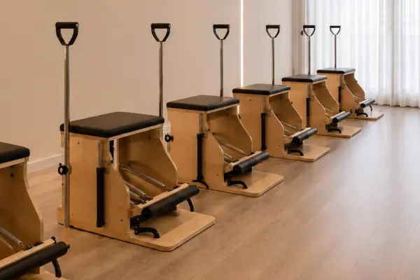 Row of wooden Pilates chair machines with black seats in a bright exercise studio.