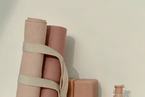 Two rolled yoga mats strapped together next to two yoga blocks and a water bottle on a beige surface.