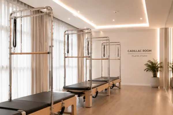 Modern Pilates studio with Cadillac reformers lined up beside large windows and light wood flooring.