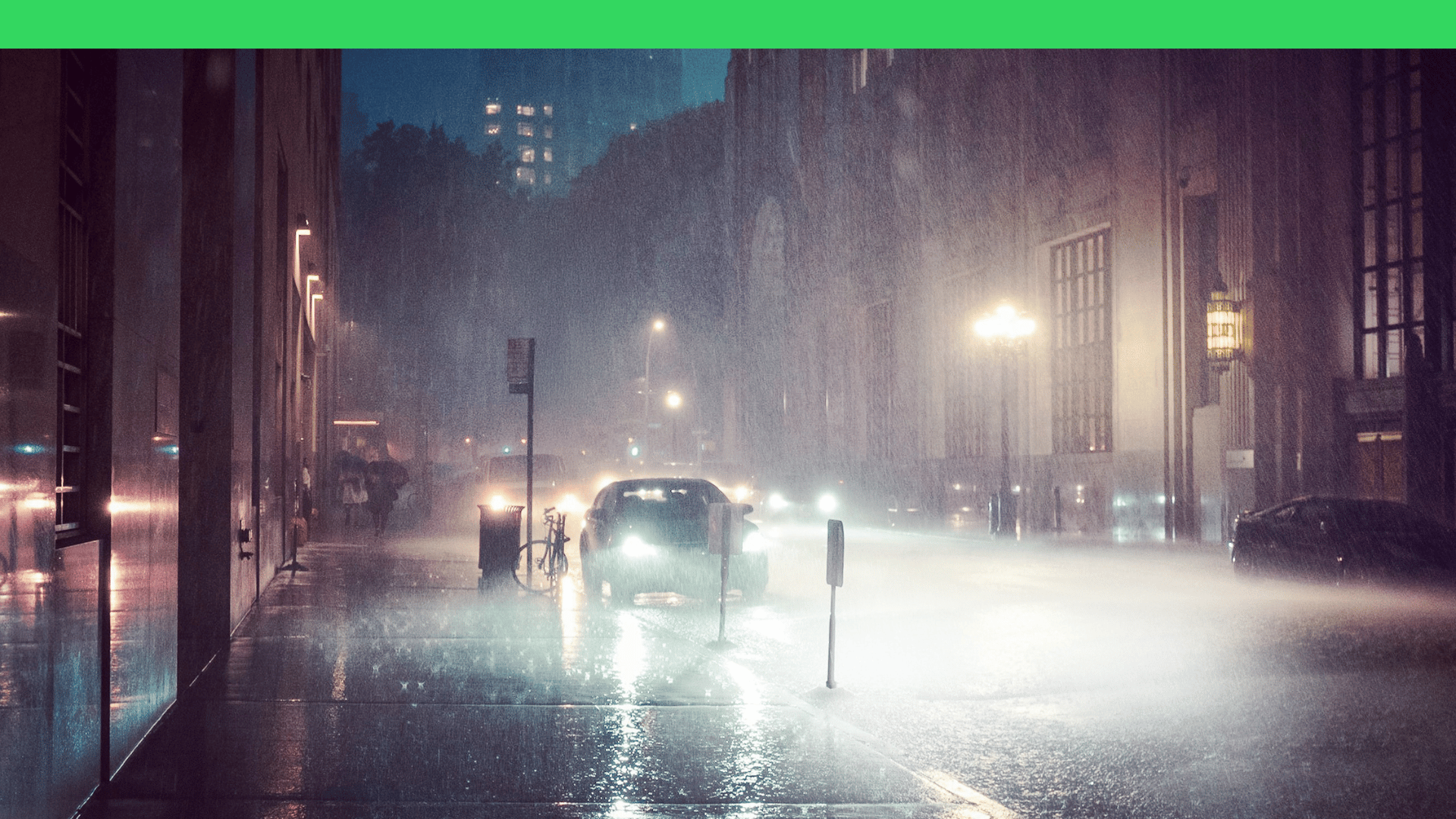 City street at night with heavy rain, headlights reflecting on wet pavement, and people holding umbrellas.
