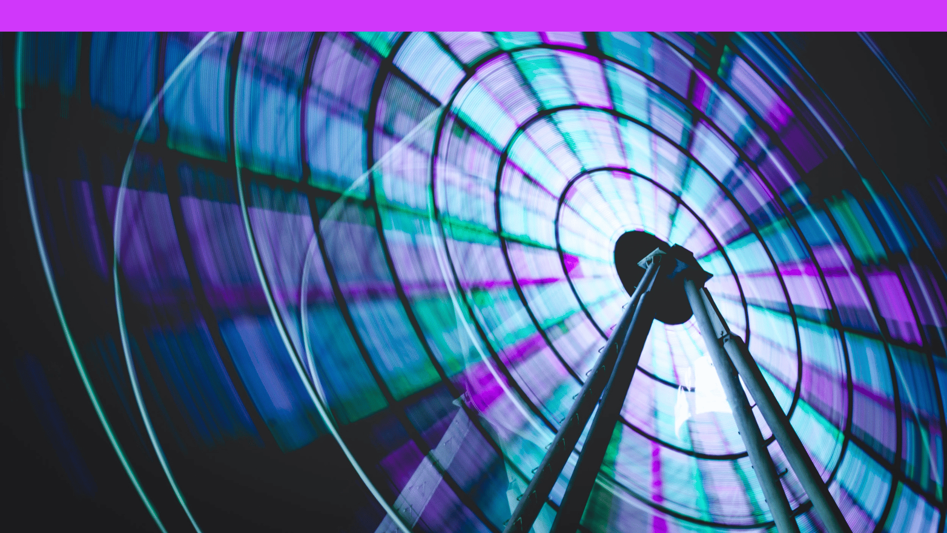 Close-up of a Ferris wheel at night with spinning blue and purple lights creating a circular motion blur.