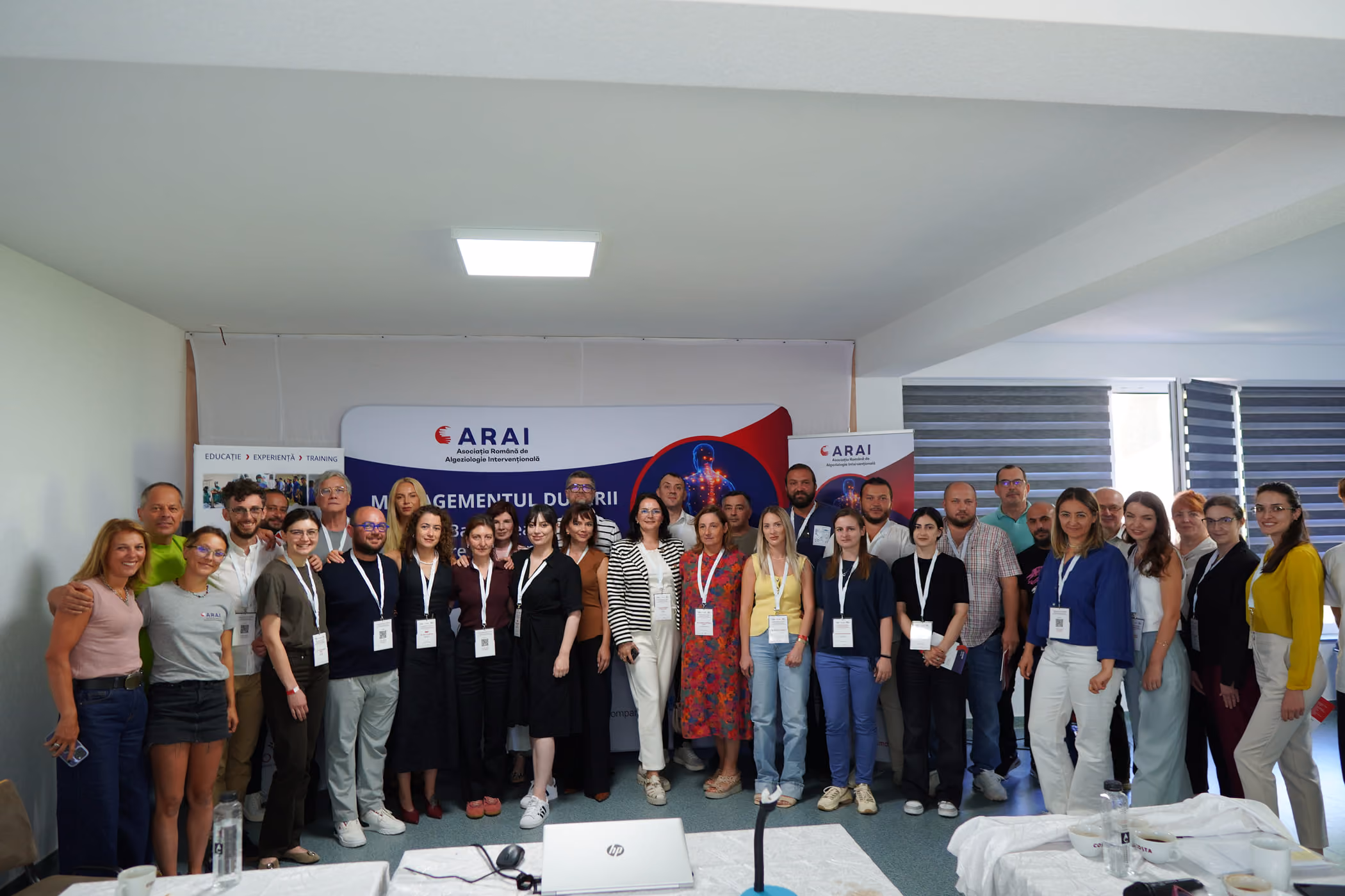 Un grup de 12 persoane poartă tricouri gri la congres sub un banner cu text și logo-uri.
