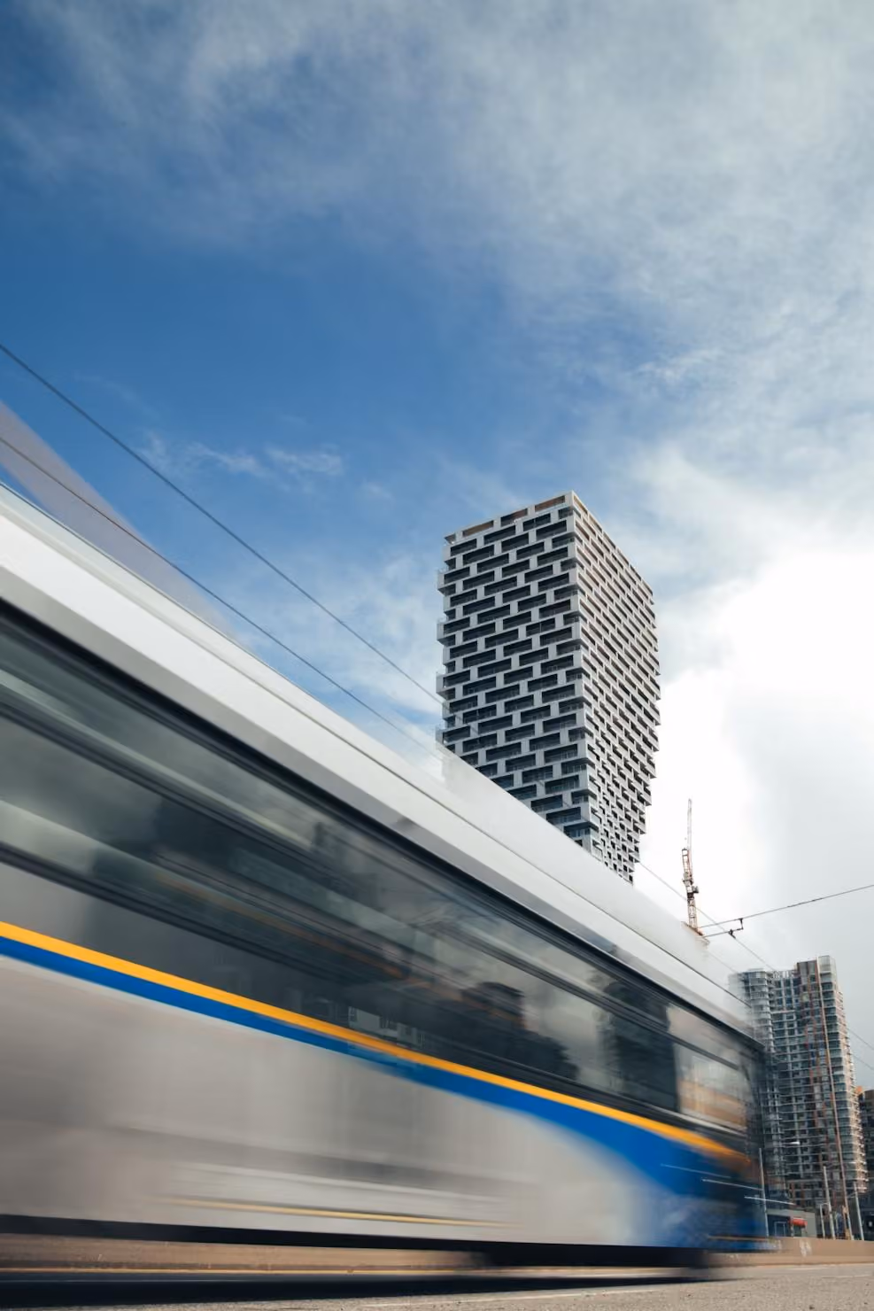Blurred city bus passing in front of a uniquely patterned modern high-rise building under a partly cloudy blue sky.